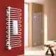 Weißer Kermi-Designheizkörper mit mehreren horizontalen Rohren, an einer roten Wand montiert. Handtuch hängt daran. Dusche mit Glasabtrennung im Hintergrund sichtbar.
